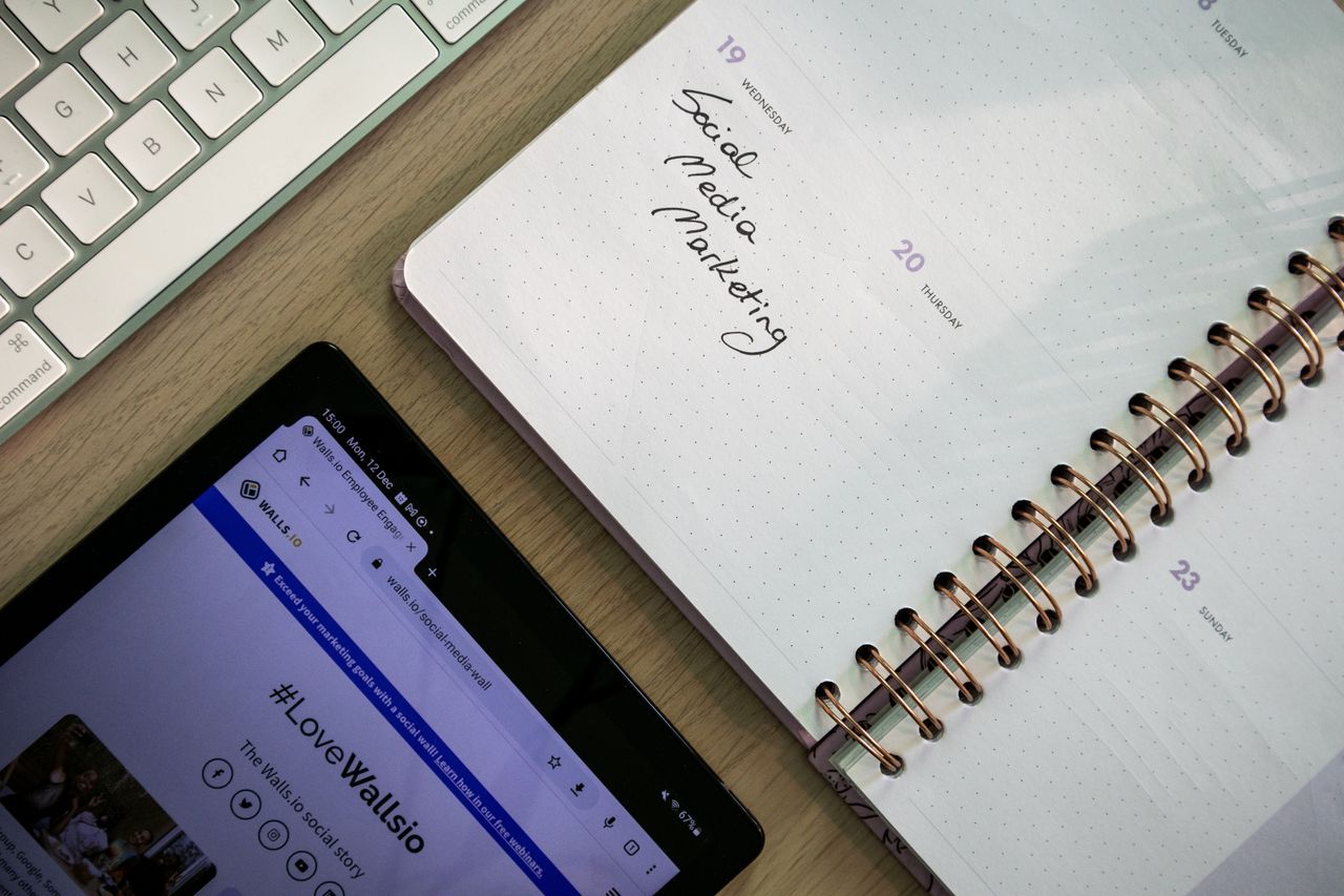 Vue plongeante d'un carnet, d'une tablette et d'un clavier employés pour la planification du marketing sur les réseaux sociaux.